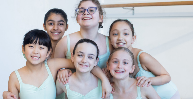  A group of student dancers, all wearing mint green leotards, are posing for a photo. They are smiling and embracing together, showcasing a sense of camaraderie and excitement.