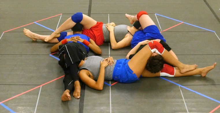 four symmetrically interconnected bodies, each with a knee draped over the neighboring forehead, providing an eye shade