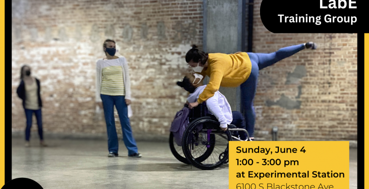 Two dancers, one using a wheelchair, practice a movement with two observers in the background