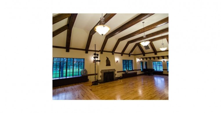 A panoramic view of the Indian Boundary Cultural Center auditorium, where the work-in-progress showing will take place. The room has a soaring ceiling lined with timber that matches the wood floors below. Windows around the perimeter show the lush park. 