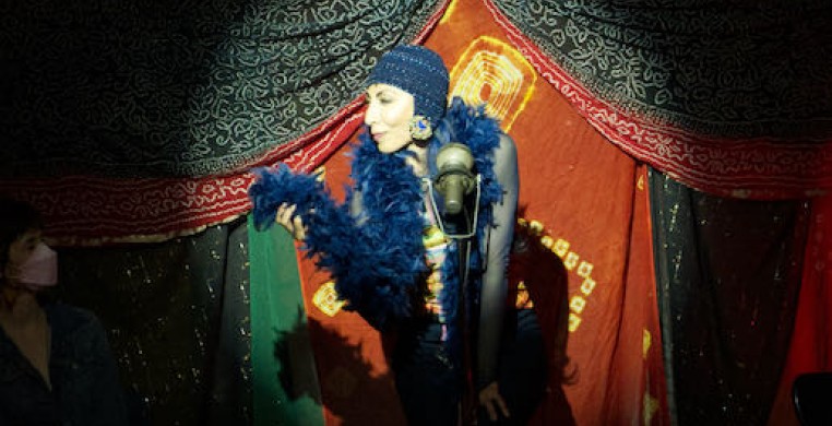 Performer seated in a spot light and holding a feather boa in hand 