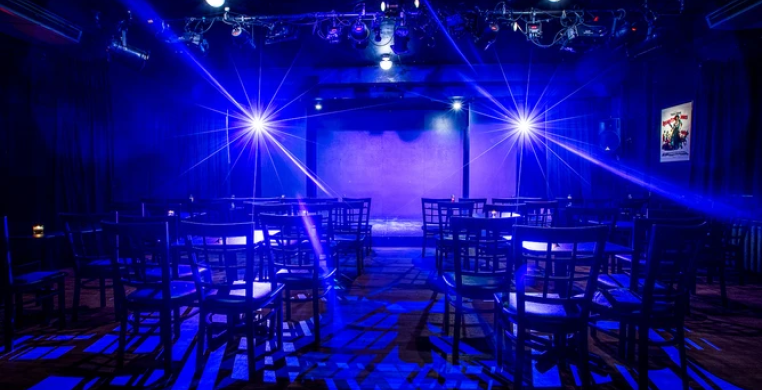 Interior of a theater with seats. Blue lights illuminate the stage.