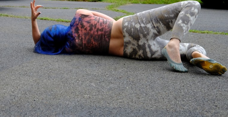 Asimina Chremos who is wearing blue wig and casual clothing lying down on the concrete 