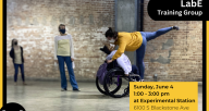 Two dancers, one using a wheelchair, practice a movement with two observers in the background