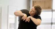 Kristina Fluty is demonstrating a dance move. Her torso slightly tilted to the side. Outer parts of her hands are touching in front of her chest.