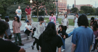 A genuine moment of Artists being in space with one another and finding ways to make it work with the respective differences. Some are sitting, some are dancing, some are standing and engaging in different ways. They are outside on concrete area of a park